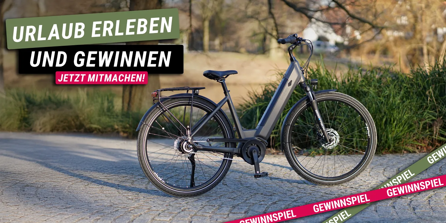 Geniesser 3.3 E‑Bike steht auf einem gepflasterten Weg im Grünen, daneben Text „Urlaub erleben und gewinnen – jetzt mitmachen