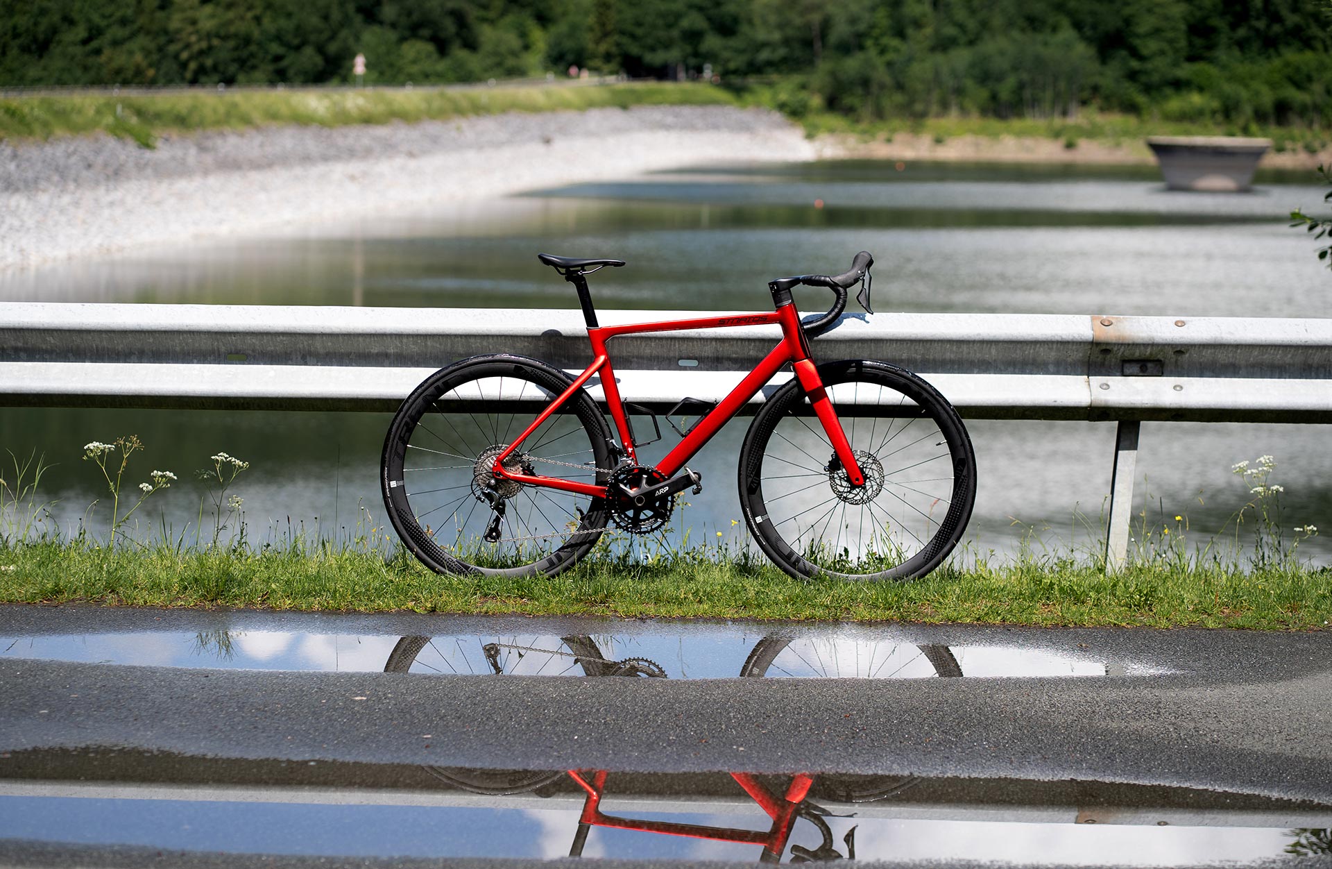 Rotes Stratos Rennrad steht an der Straße vor einer Pfütze