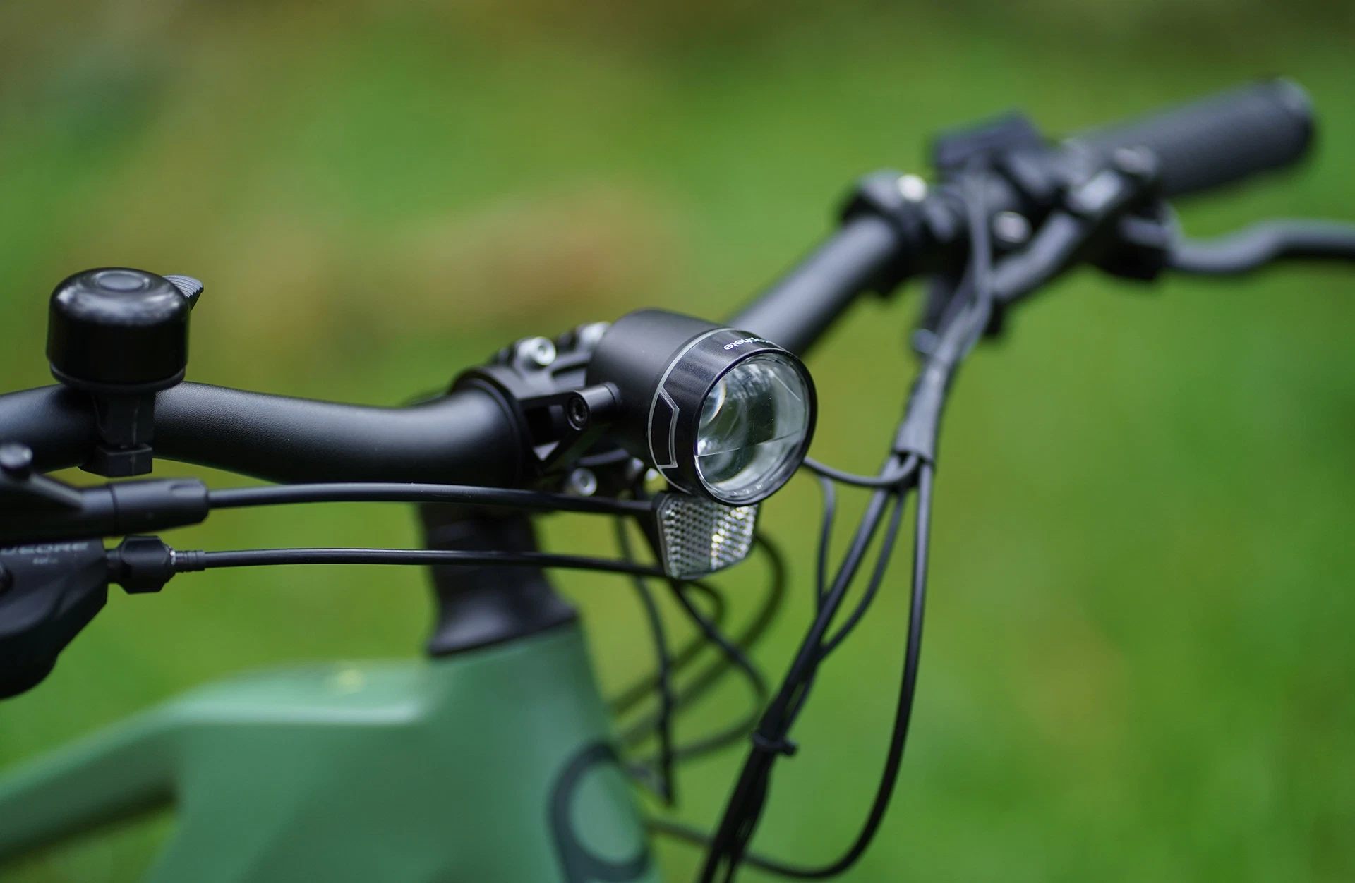 Bildausschnitt Lenker mit Scheinwerfer, Klingel und Reflektor vor unscharfem Hintergrund