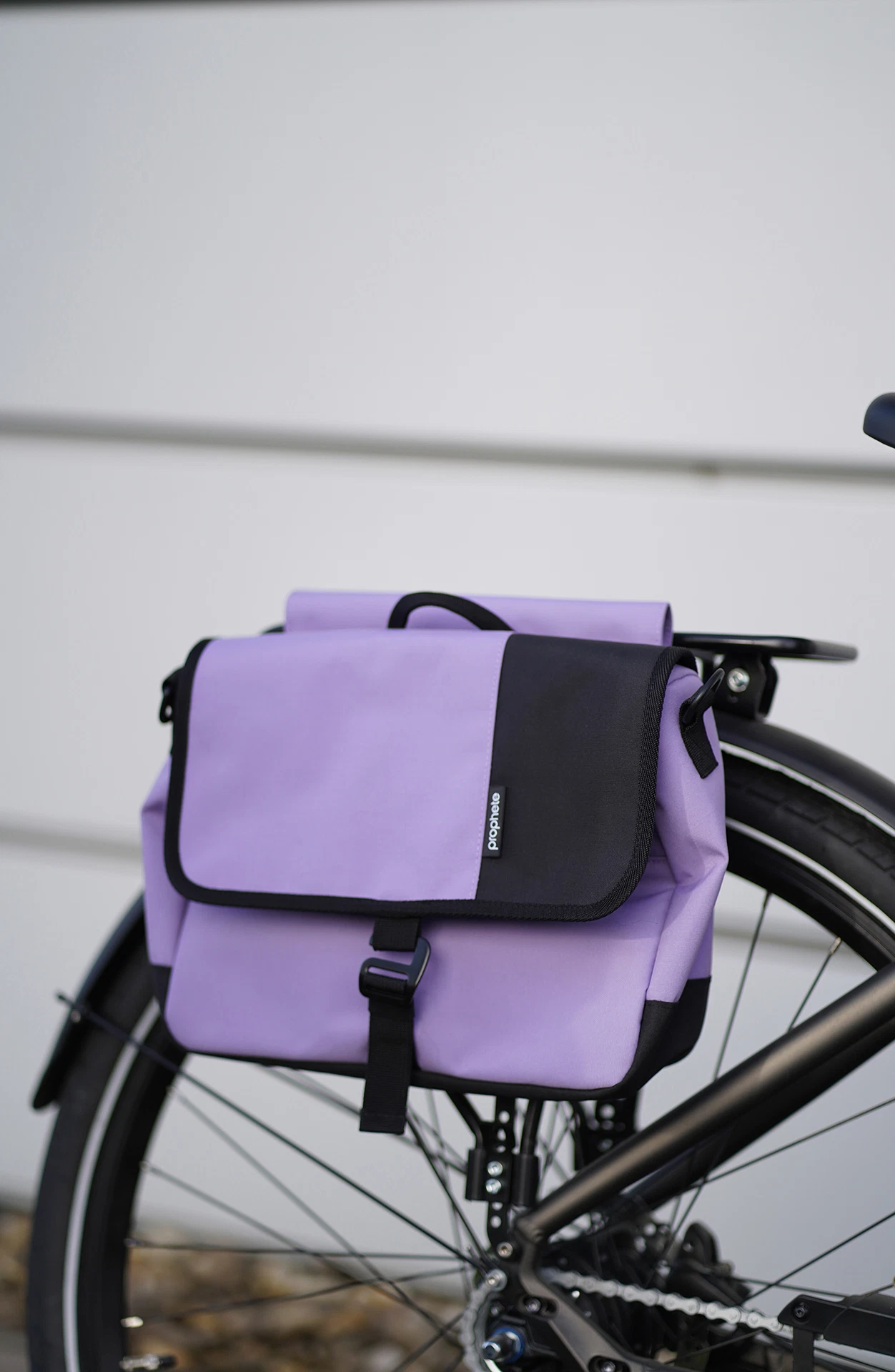 Vollansicht frontal Packtasche in lila mit schwarzen Applikationen vor Fassade im Hintergrund