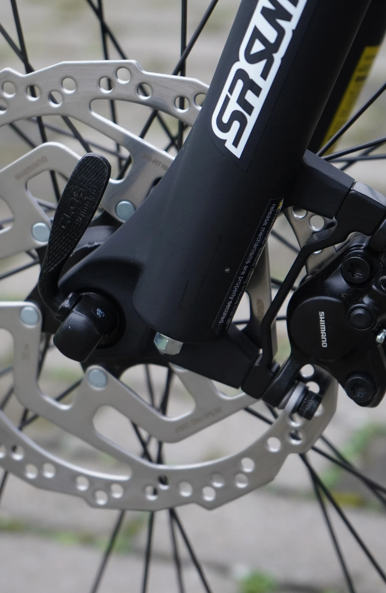 Vorderrad mit Scheibenbremse, Shimano-Bremszange, Suntour XCT30-Federgabel und Bremsscheibe vor grauem Pflaster