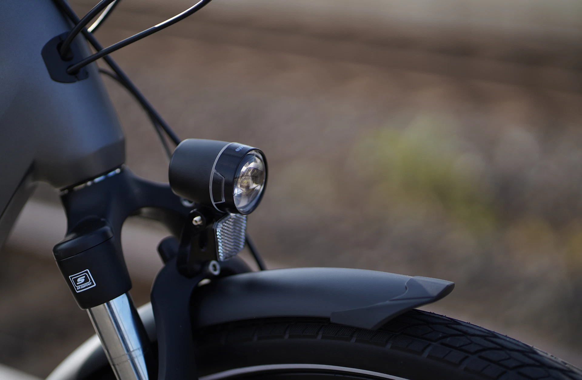 Bildausschnitt Detailansicht Scheinwerfer mit Reflektor, Federgabel, Schutzblech und Reifen im Anschnitt vor unscharfem Hintergrund