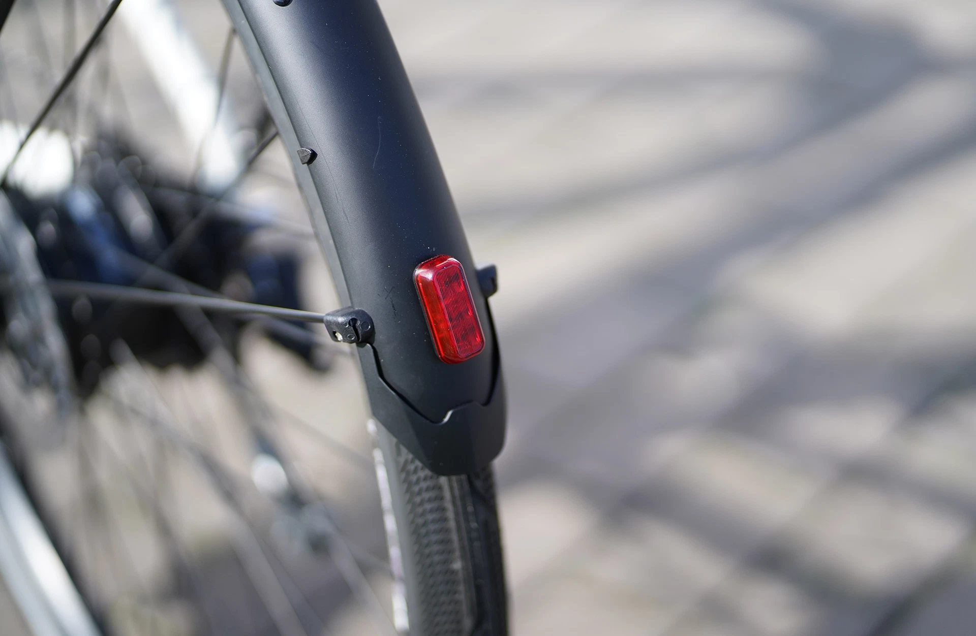 Bildausschnitt Hinterrad mit Schutzblech und integriertem Rücklicht auf unscharfem gepflasterten Untergrund