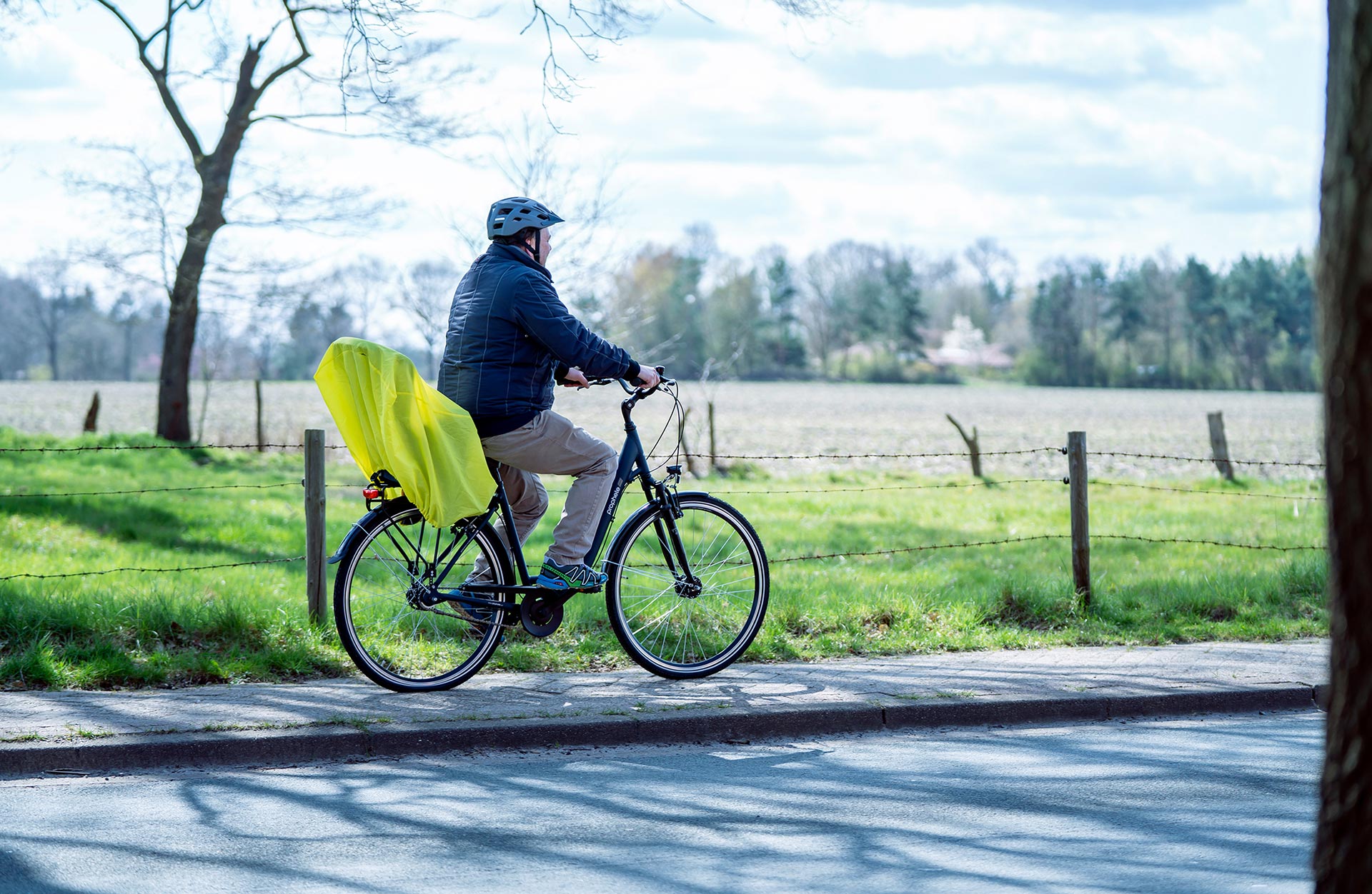 Kindersitzregenüberzug montiert auf Cityrad von einem Mann gefahren - Seitensicht vor Feld