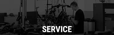 Mechaniker arbeitet an einem Fahrrad, im Vordergrund steht der Schriftzug ‚Service‘