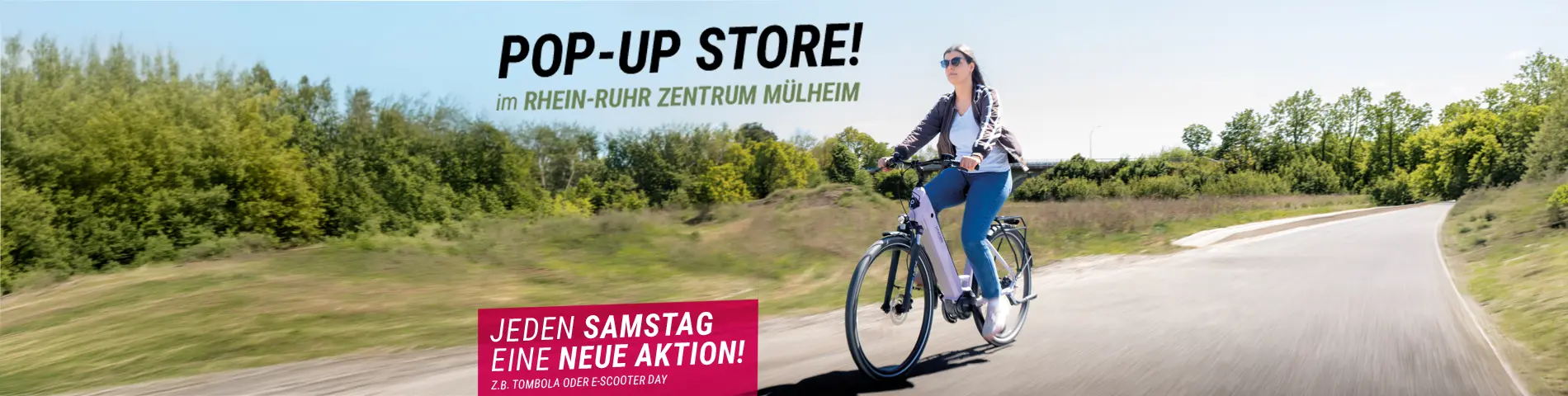Person fährt mit einem E‑Bike auf einem Weg im Grünen, Werbung für Pop-up Store im Rhein-Ruhr Zentrum Mülheim mit Hinweis, Jeden Samstag eine neue Aktion.