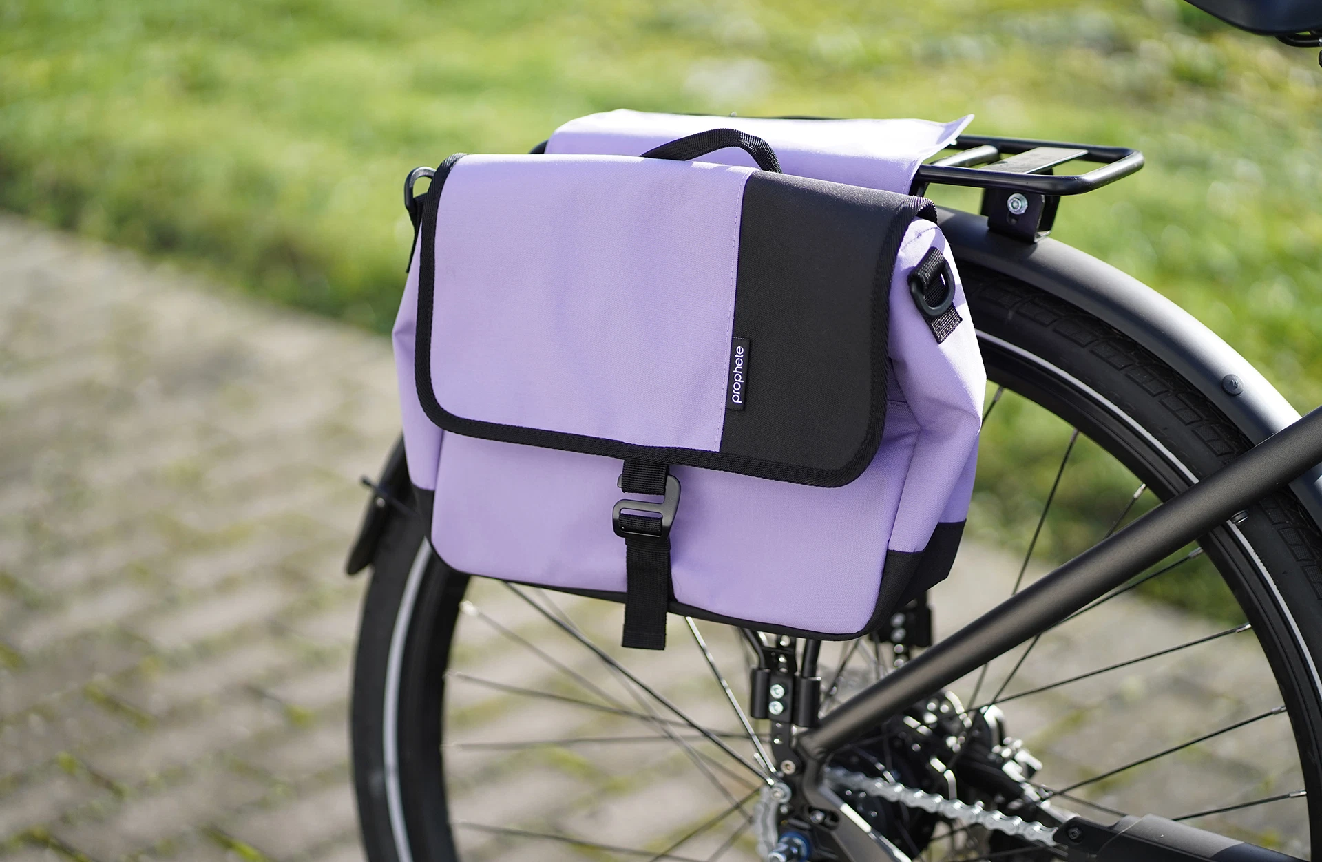 Vollansicht lila Seitenpacktasche am Heckgepäckträger mit gepflastertem Untergrund und Rasen