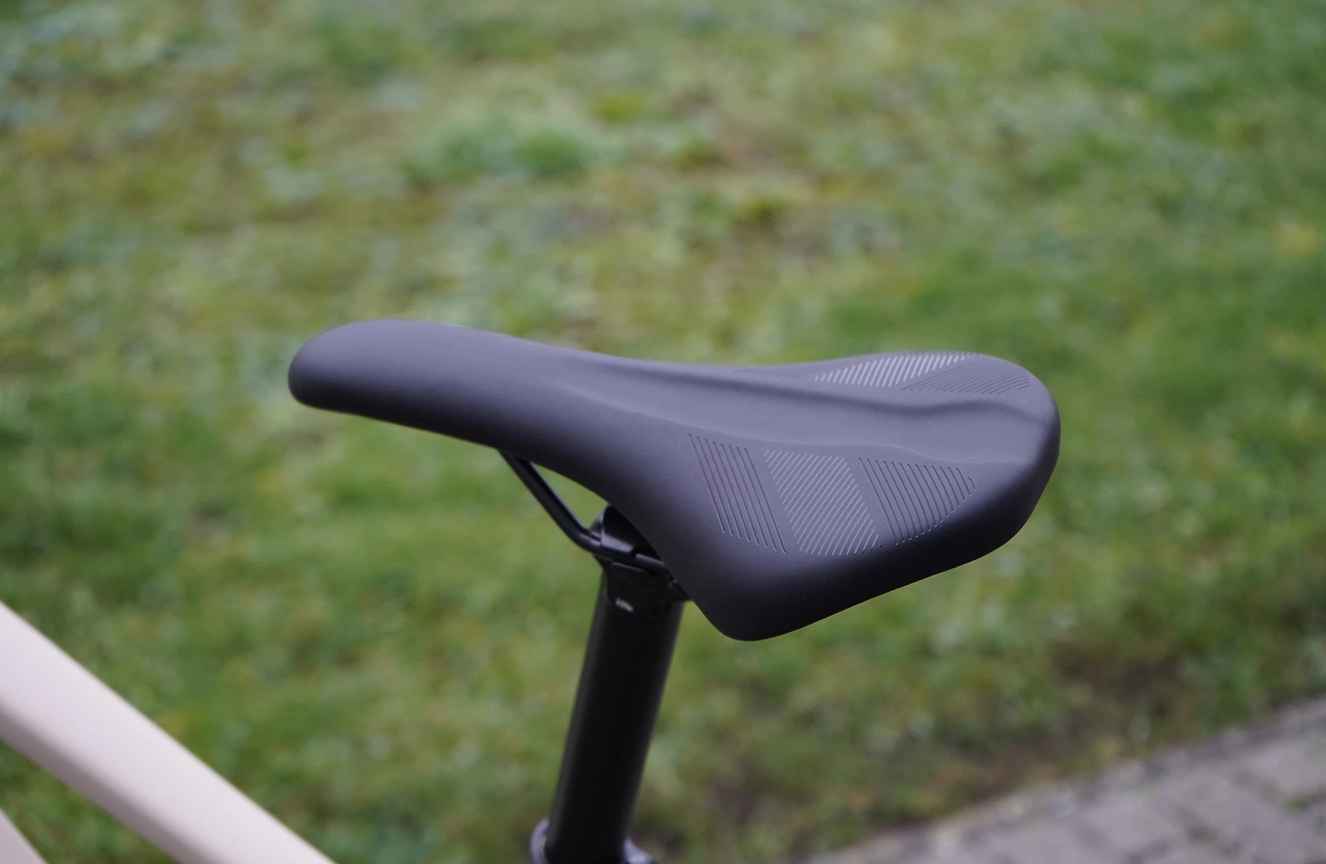 Schwarzer Fahrradsattel mit dezentem Muster auf schwarzer Sattelstütze, grüner Rasen unscharf im Hintergrund