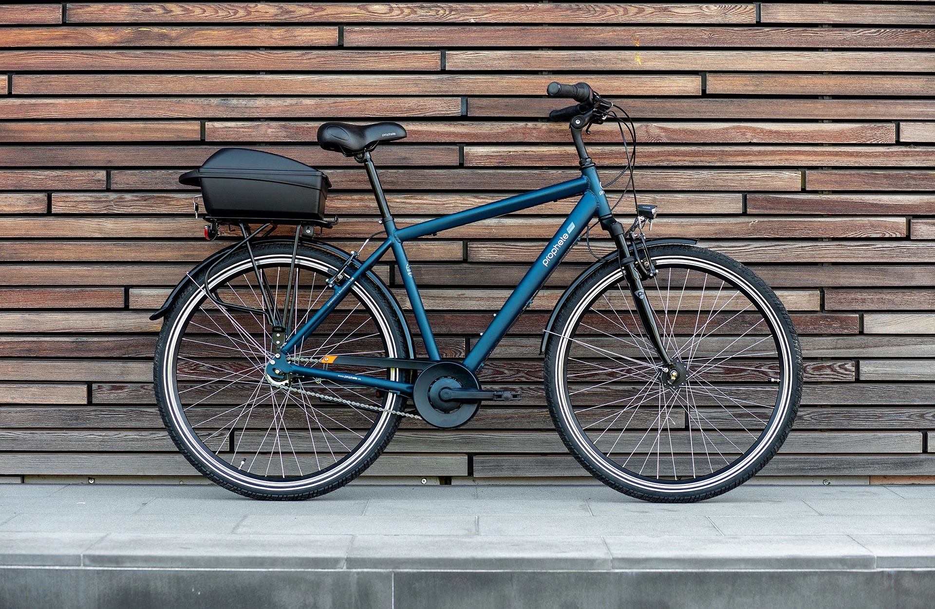 Seitliche Ansicht Fahrrad mit Gepäckträgerbox auf dem Gepäckträger vor stylischer Wand
