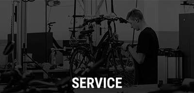 Werkstattmitarbeiter repariert ein Fahrrad, im Vordergrund steht der Text ‚Service‘