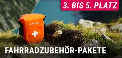 Orange Erste-Hilfe-Tasche mit weißem Kreuz liegt in einer Berglandschaft, Text Fahrradzubehör‑Pakete und 3. bis 5. Platz