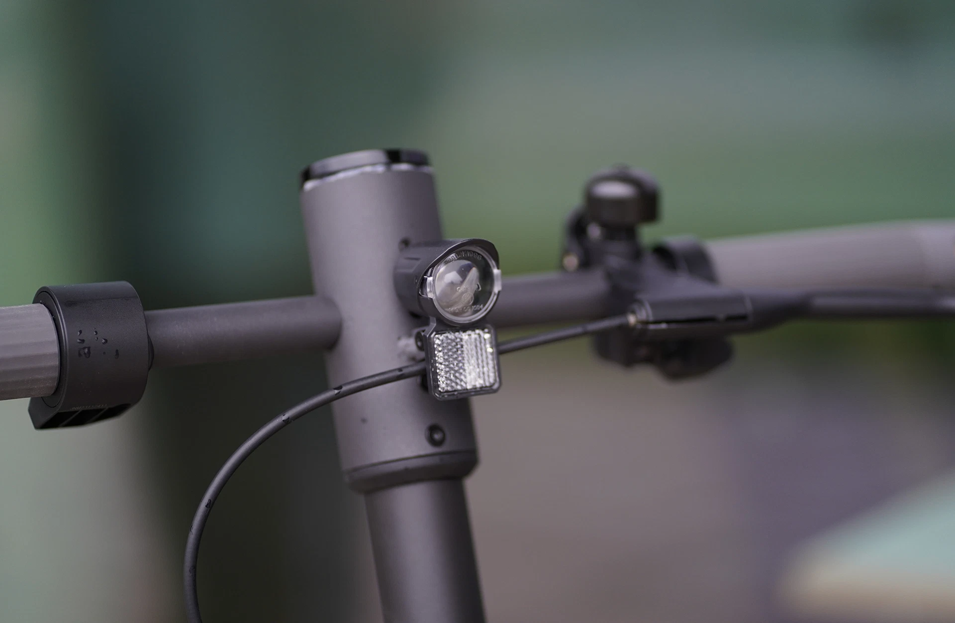 Bildausschnitt Lenker mit Scheinwerfer, Reflektor, Klingel und Bremshebel vor unscharfem Hintergrund