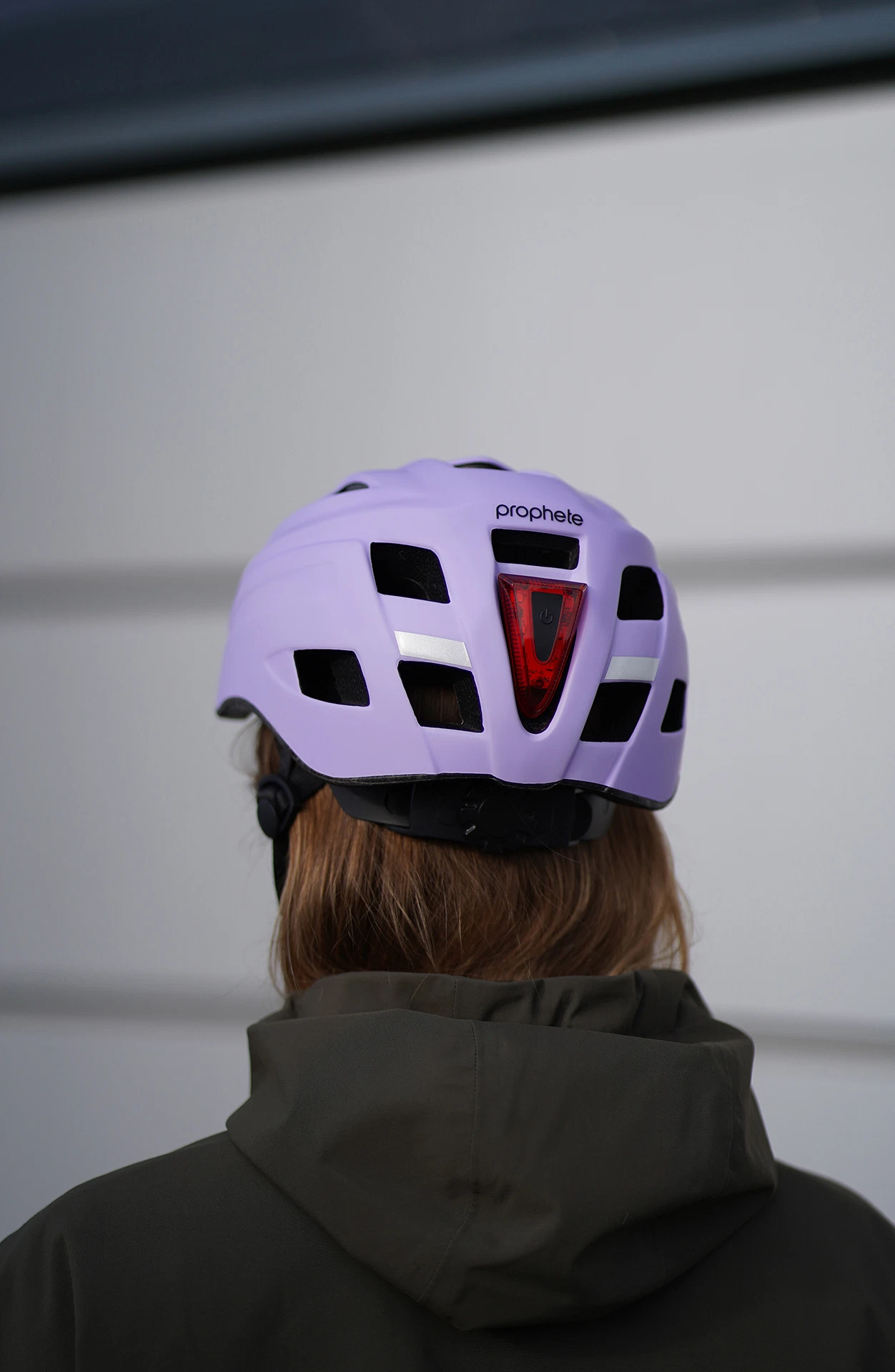 Fahrradhelm lila getragen vor einer grauen Wand - Ansicht von hinten