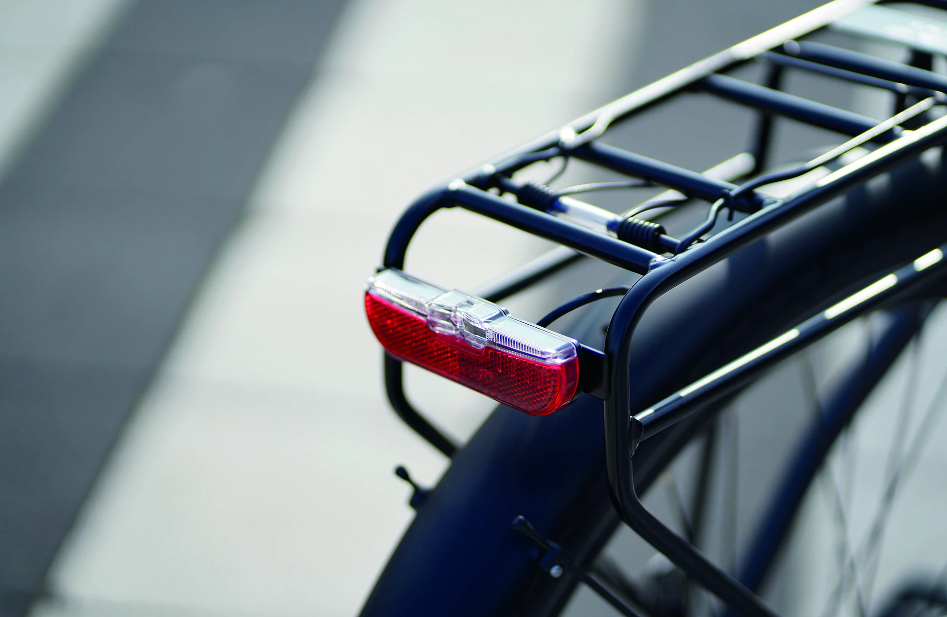 Bildausschnitt Gepäckträger schräg von hinten mit Rücklicht und Reflektor vor unscharfem, grauen Hintergrund