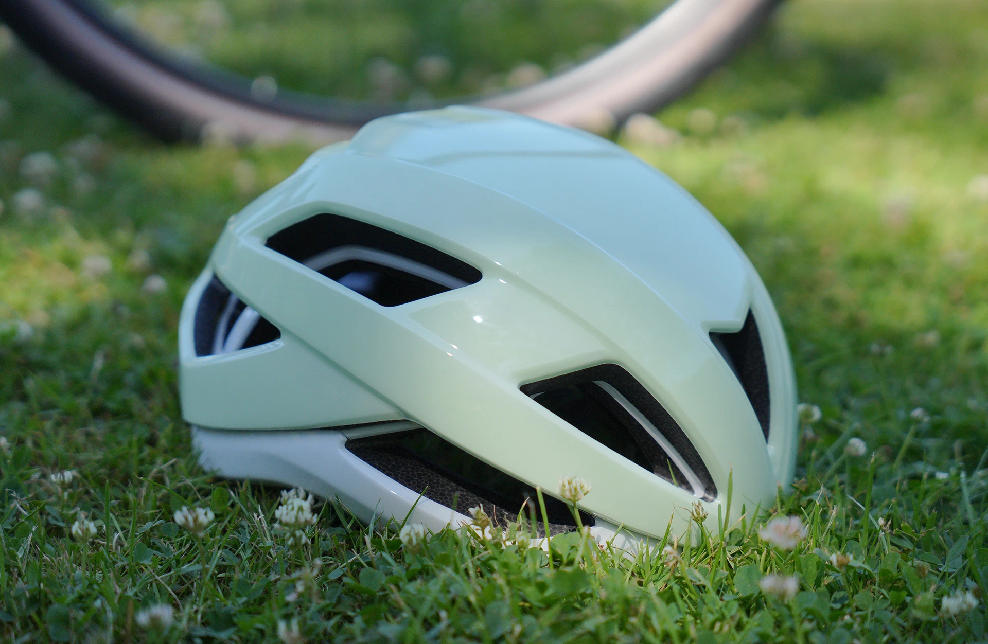 ProShield Fahrradhelm auf Rasenfläche mit Fahrradreifen im Hintergrund - diagonal