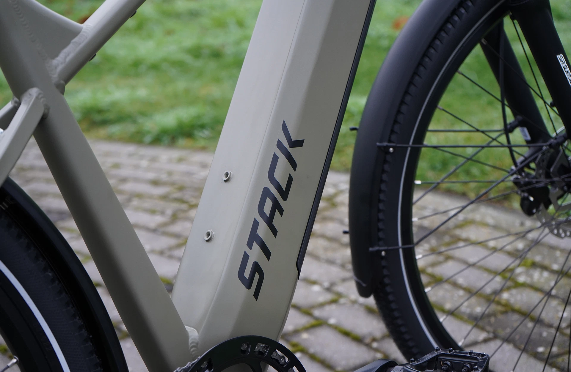 Bildausschnitt Rahmen des Prophete Stack mit Logodruck, integriertem Akku im Unterrohr und angeschnittenem Vorderreifen auf gepflastertem Untergrund und Rasen