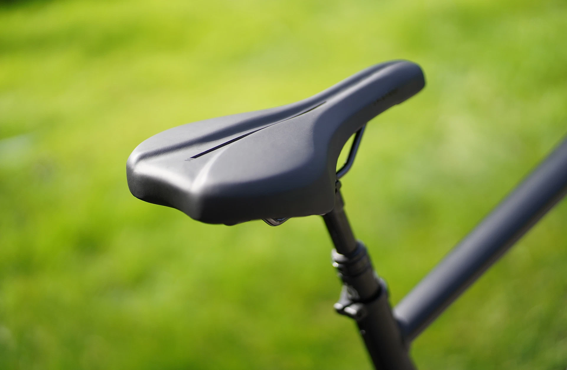 Bildausschnitt Detailansicht Sattel schräg von hinten, oben fotografiert mit Sattelstütze und Oberrohr, sowie unscharfem Rasen im Hintergrund