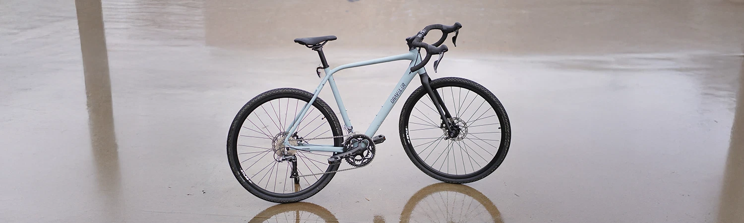 Vollansicht seitlich Prophete Graveler Bike auf asphaltiertem Weg mit Wasser auf dem Untergrund
