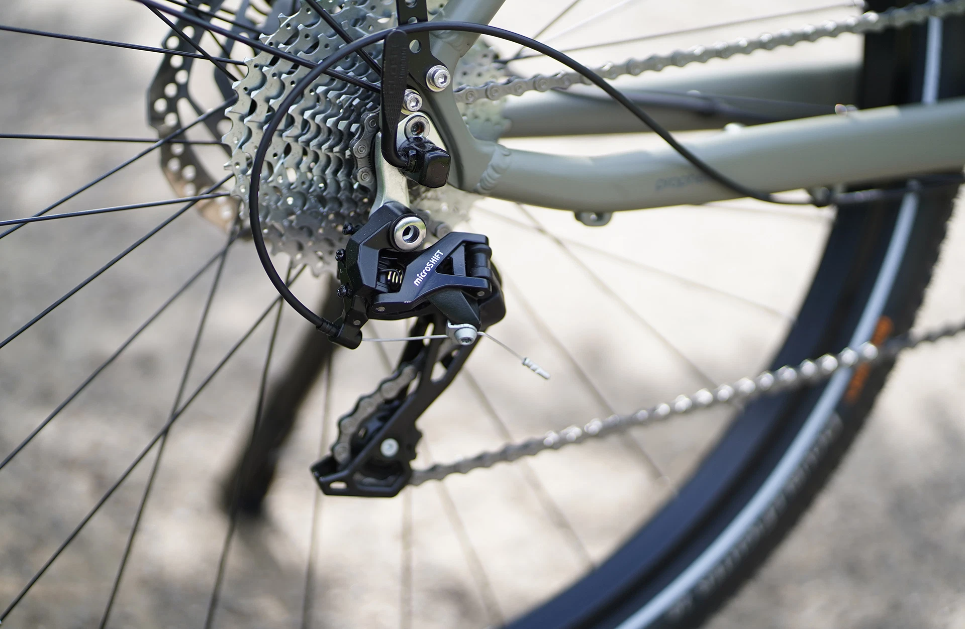 Bildausschnitt Detailaufnahme Microshift Schaltwerk mit Kette und Kassette am Hinterrad vor unscharfem, grauem Untergrund