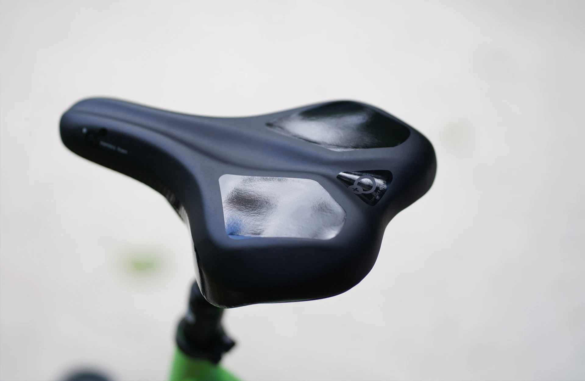 Nahaufnahme eines schwarzen Fahrradsattels mit zwei reflektierenden Flächen – eine größere und eine kleinere – vor neutralem Hintergrund