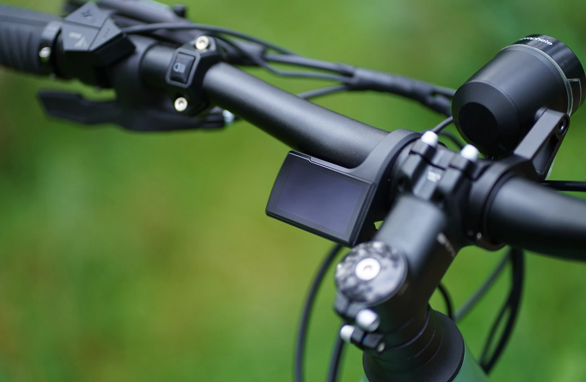 Bildausschnitt Lenker mit ausgeschaltetem TFT Display neben dem A-Head Vorbau und Bedieneinheiten neben dem Griff vor unscharfem Hintergrund