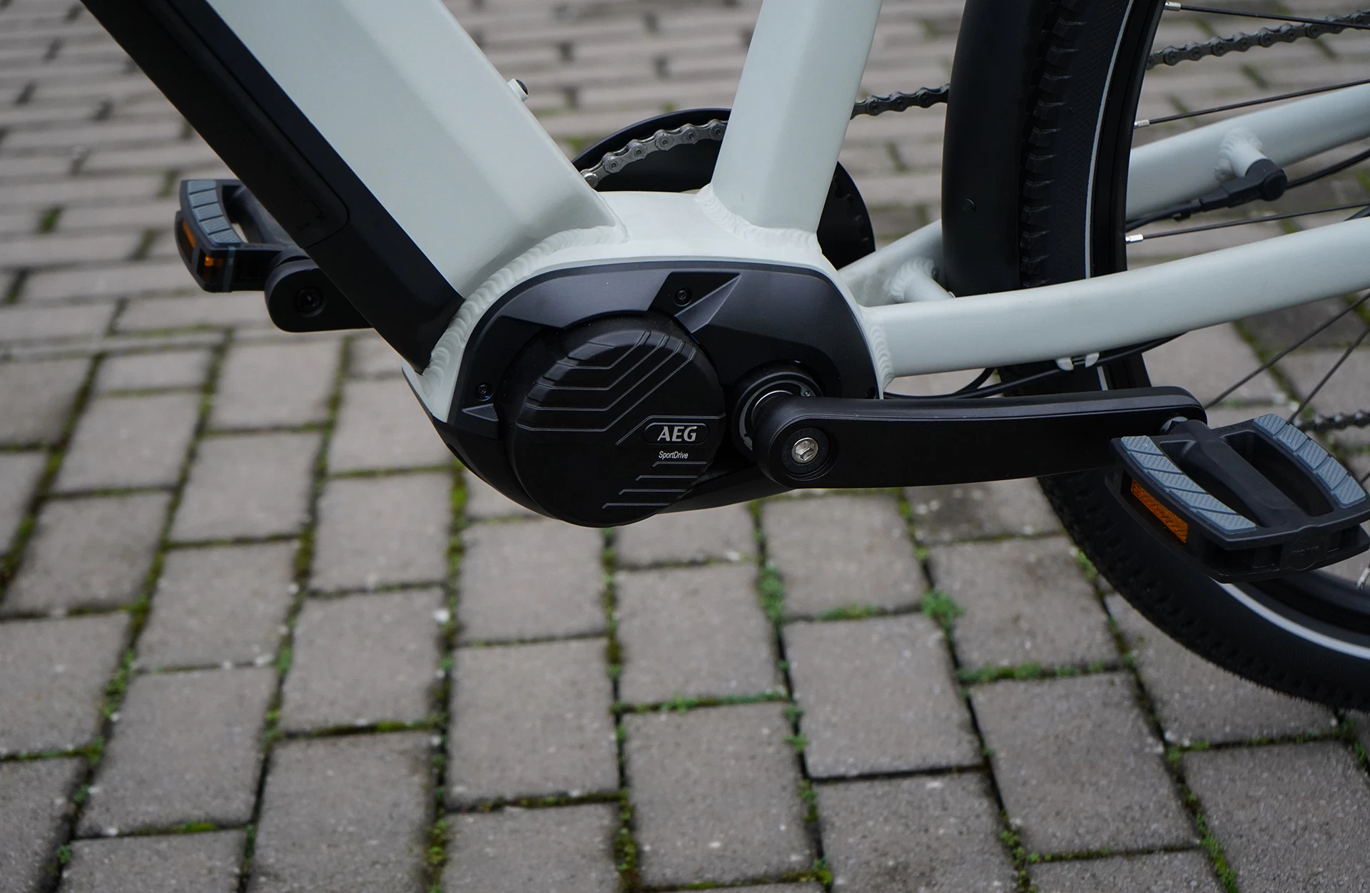 Bildausschnitt Mittelmotor von AEG mit Kurbel und Pedalen auf gepflastertem Untergrund