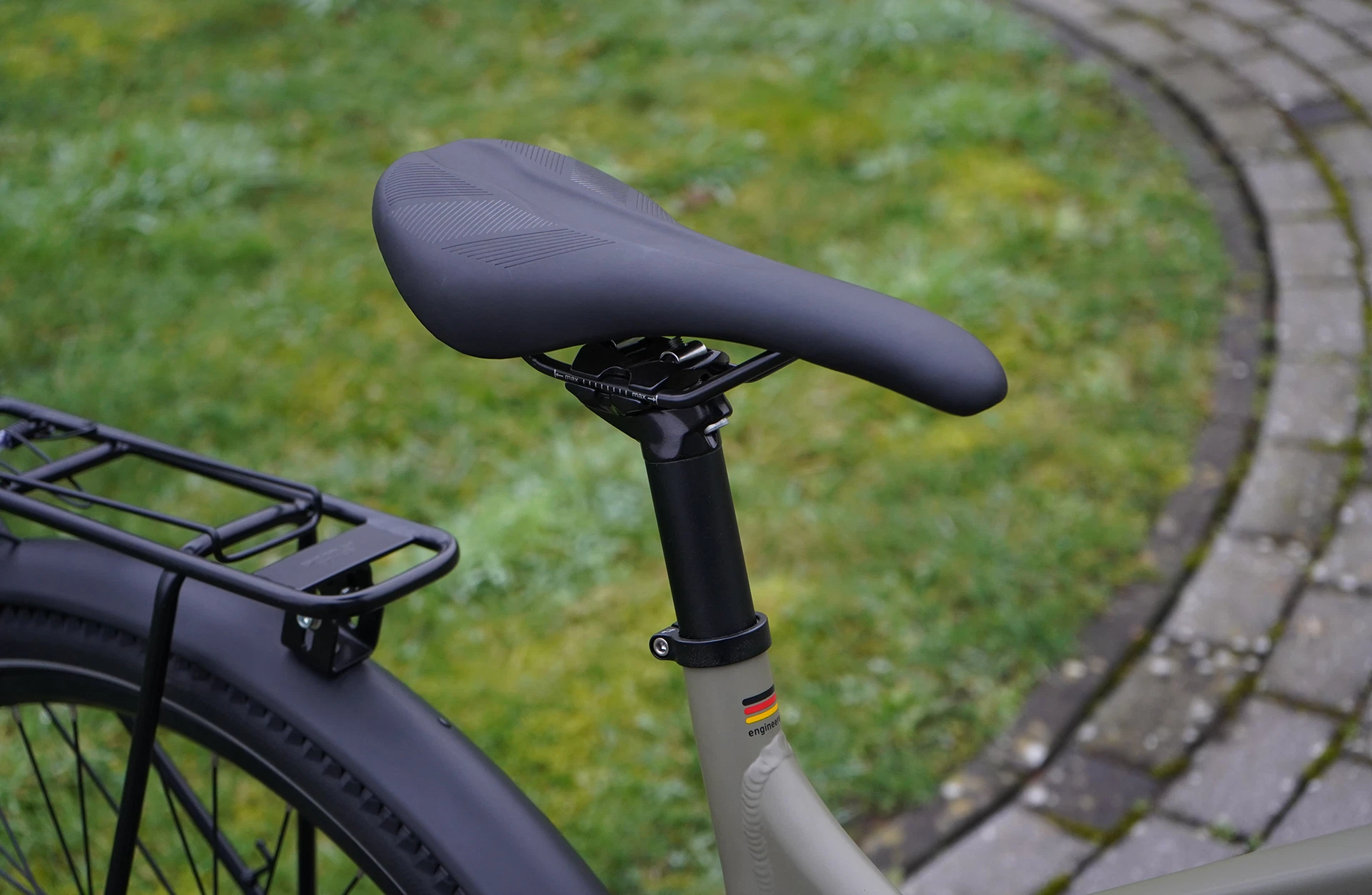 Bildausschnitt sportlicher Sattel auf schwarzer Sattelstütze mit Deutschlandfahne und Gepäckträger auf Schutzblech vor Rasen und Pflastersteinen