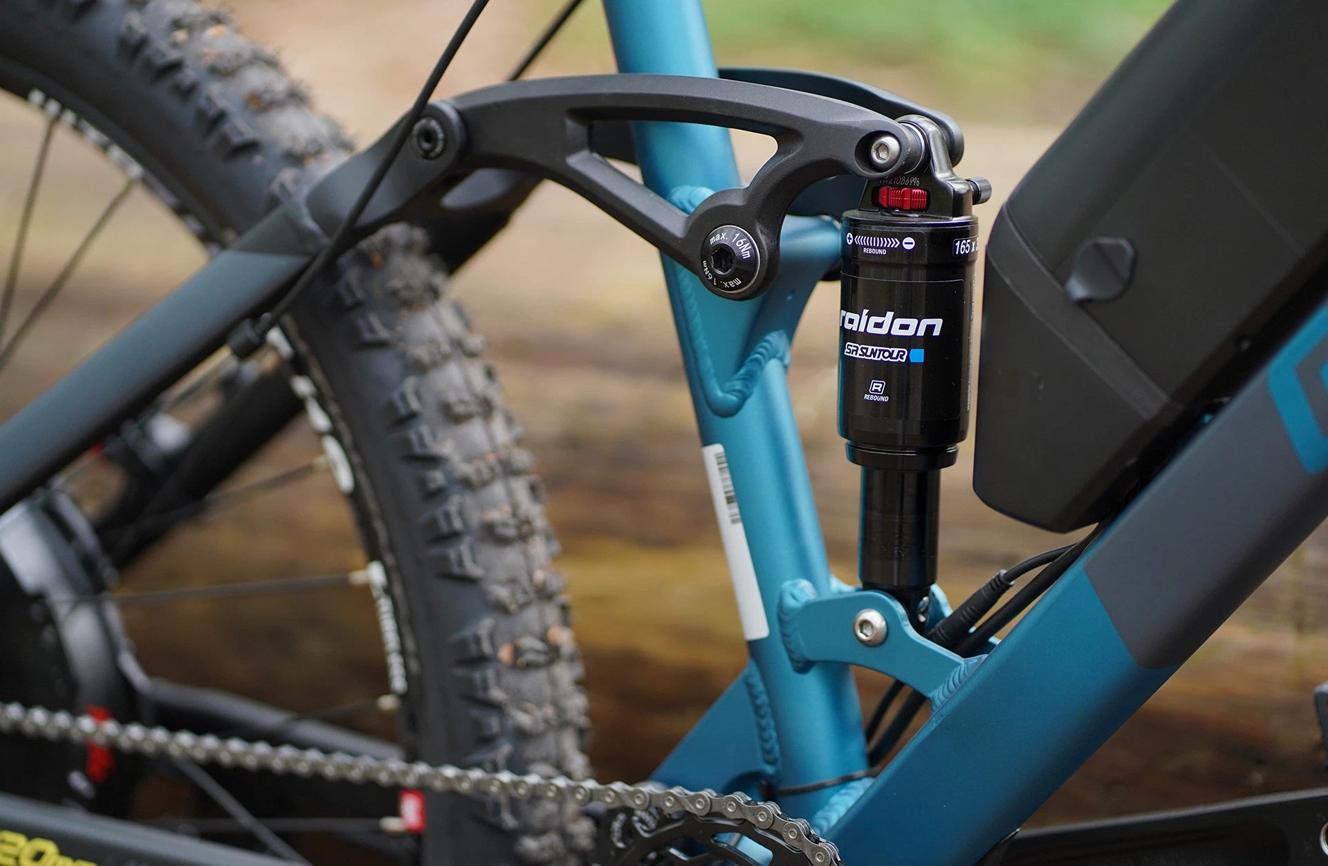 Bildausschnitt Detailansicht Dämpfer am Hinterbau und AEG Akku im Anschnitt vor unscharfem, natürlichem Hintergrund