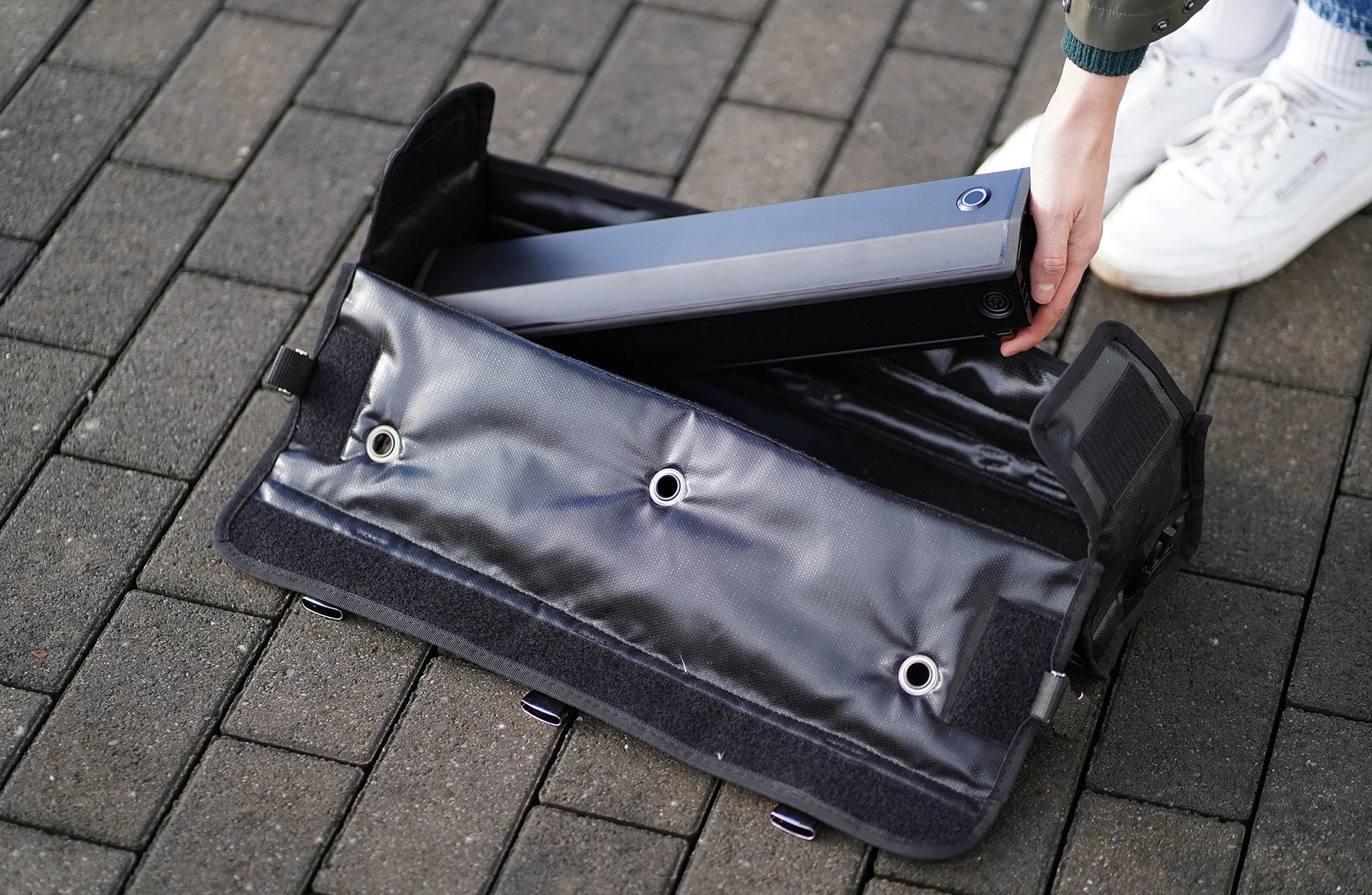 Akkutasche auf Pflastersteinen und Person legt Akku in die Tasche