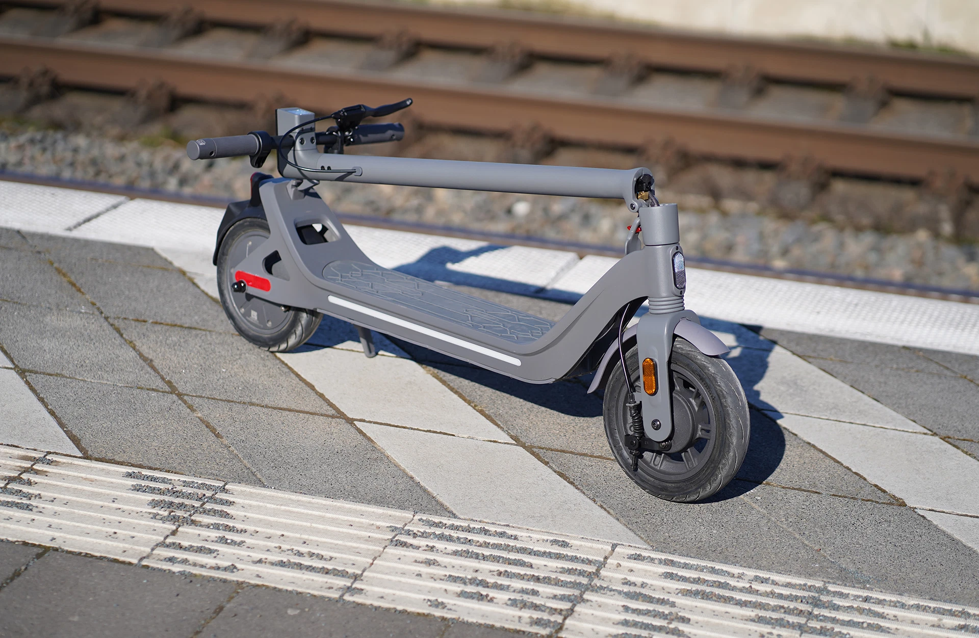 Vollansicht eingeklappter Prophete E-Scooter TWO liegend aufgestellt am Bahnsteig mit Schienen im Hintergrund