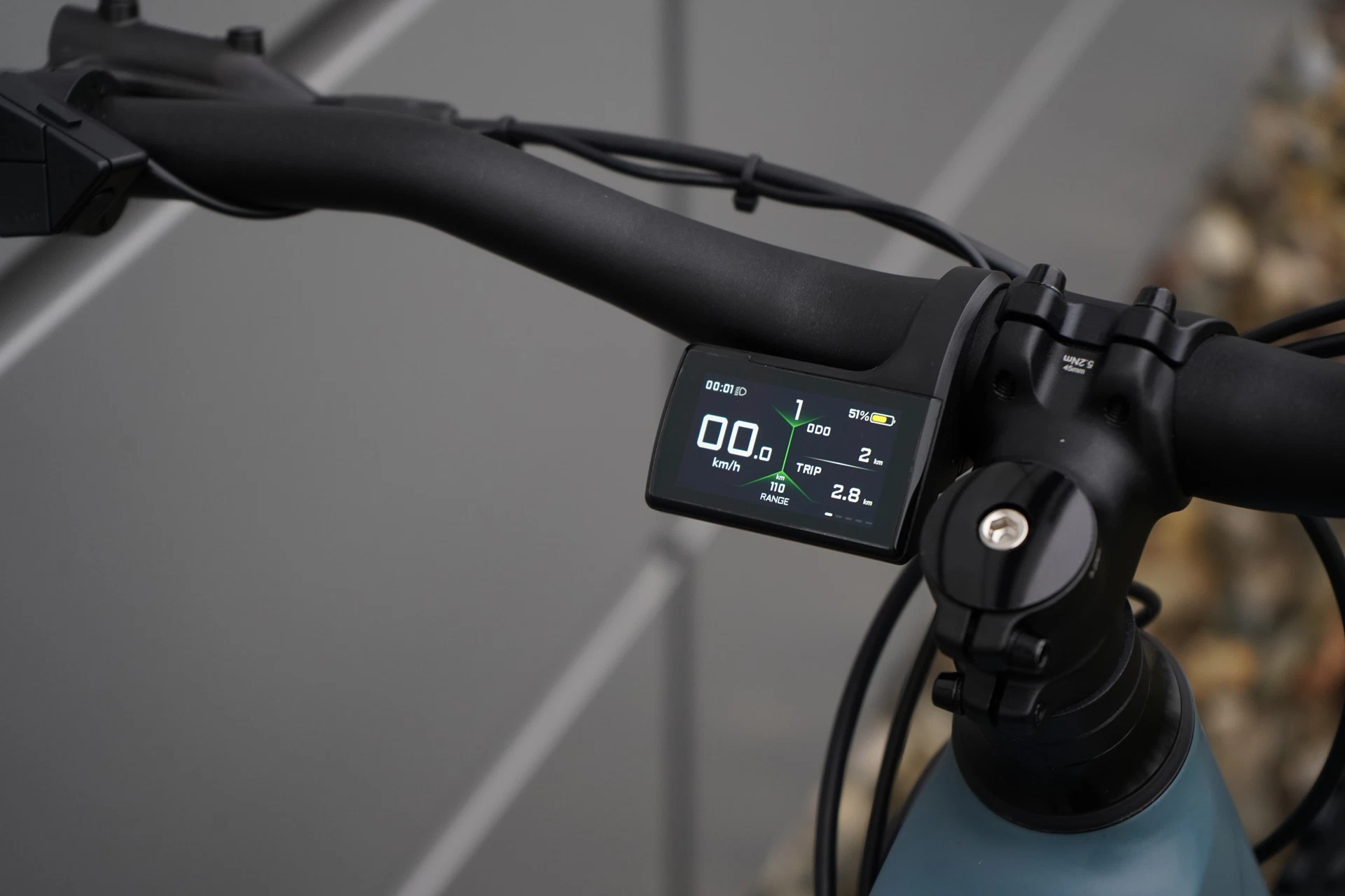 Bildausschnitt vollfarbiges TFT Display neben Vorbau am Lenker vor Metallhintergrund und auf Steinen