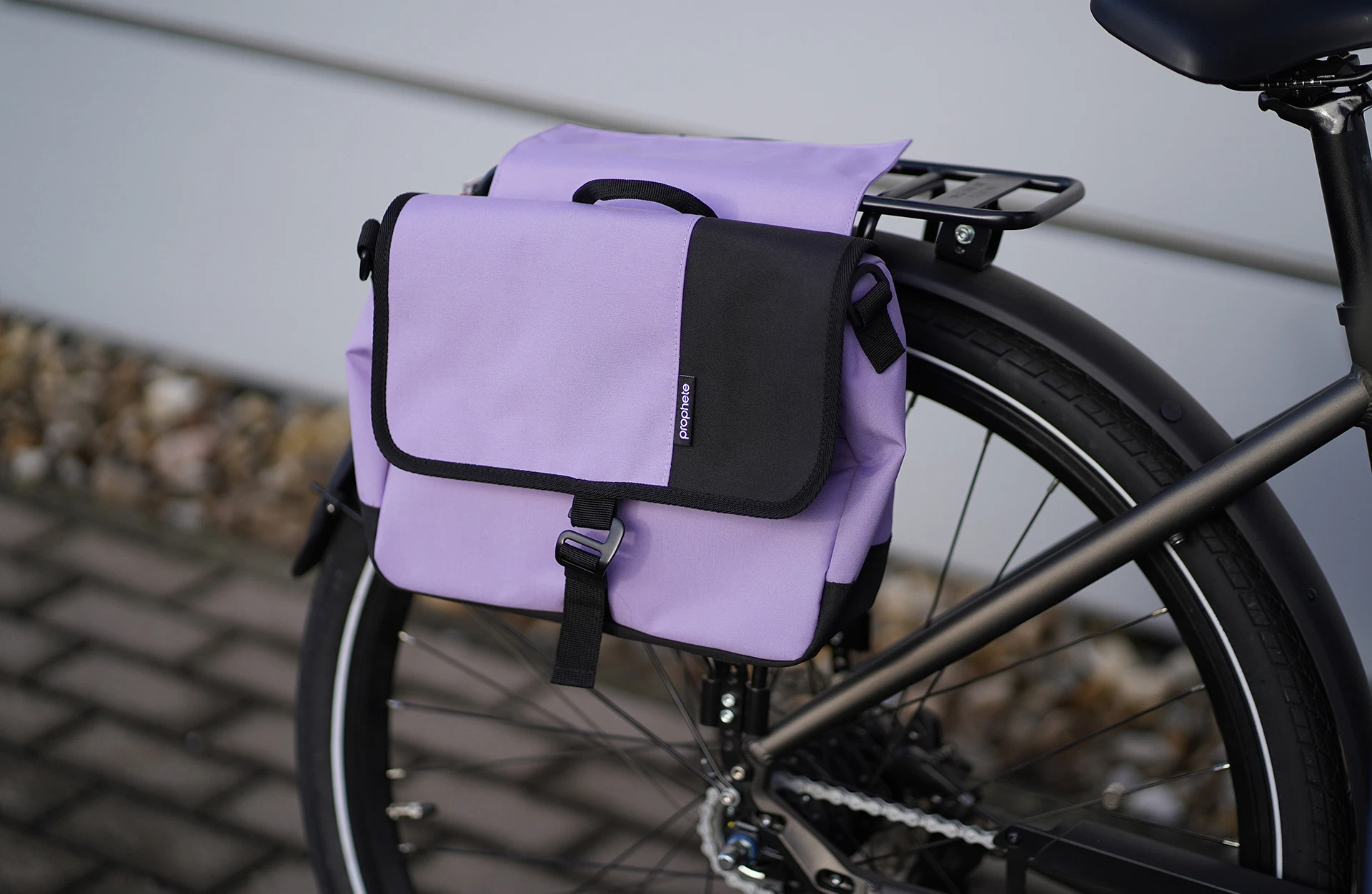 Seitenpacktasche lila am Heckgepäckträger mit Sattelrohr im Anschnitt vor Pflastersteinen und Fassade im Hintergrund