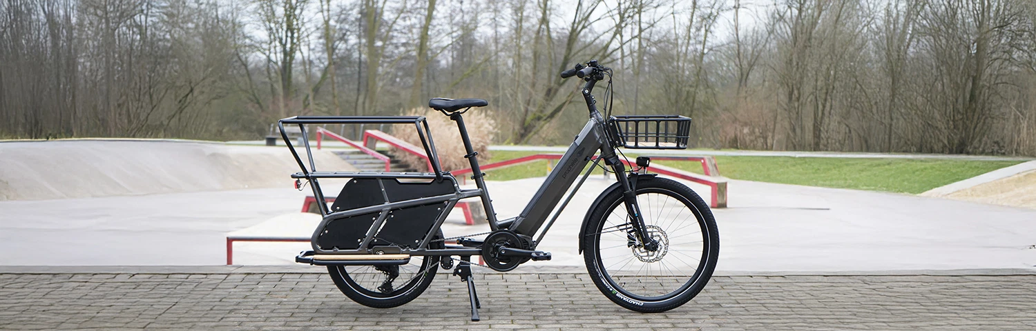 Seiten Vollansicht Prophete E-Lastenrad samt Frontkorb, Mittelmotor, großem Hinterbau und robustem Zweibeinständer