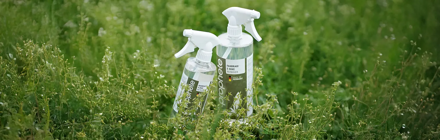 Zwei Sprühflaschen Prophete Fahrradreiniger in einer Wiese mit grünem Gras.