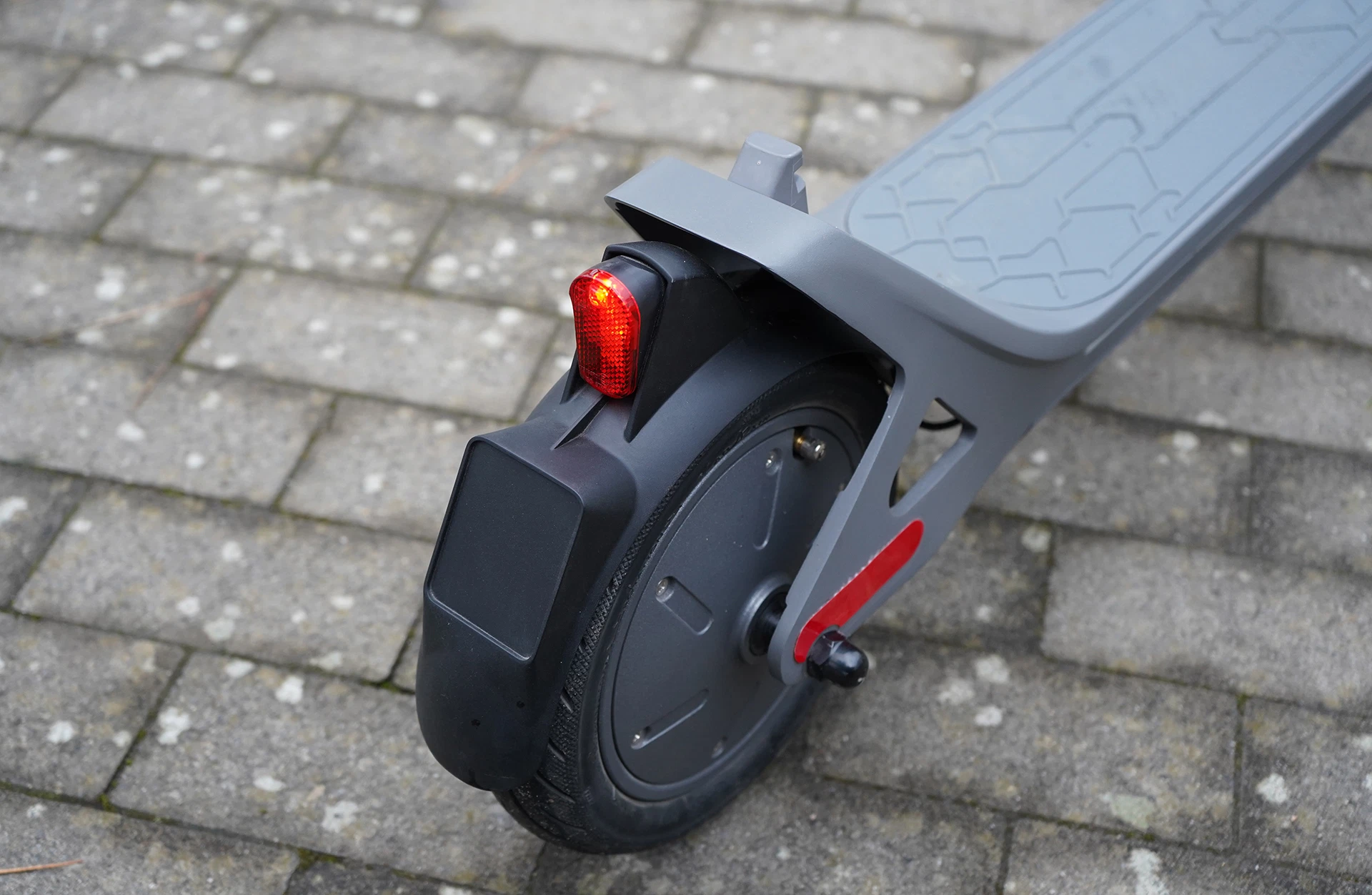 Bildausschnitt Hinterrad Prophete E-Scooter TWO mit rotem Rücklicht, grauem Trittbrett und auf Pflastersteinen