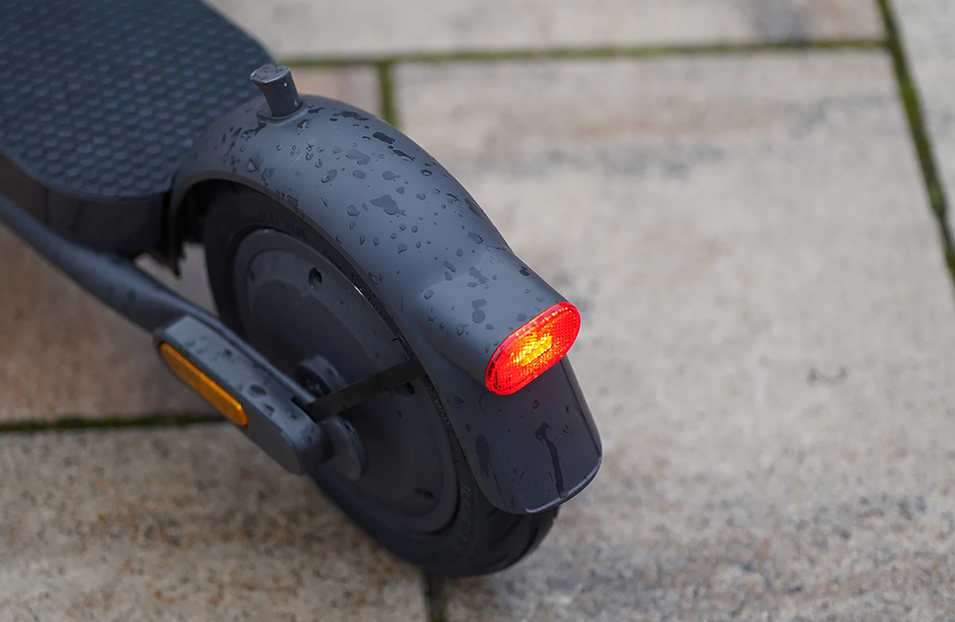 Bildausschnitt helle LED-Rückleuchte am Schutzblech und Heckmotor im Hinterrad verbaut auf gepflastertem Untergrund