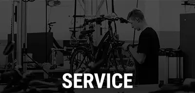 Mechaniker arbeitet an einem Fahrrad, im Vordergrund steht der Schriftzug ‚Service‘