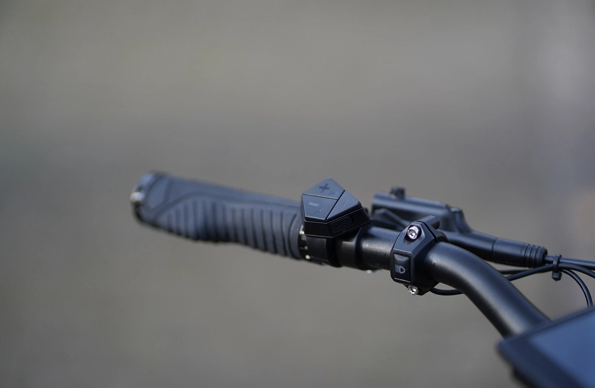 Bildausschnitt Detailansicht linker Griff (geschraubt) mit Bedieneinheit und Bremshebel vor unscharfem, grauem Hintergrund