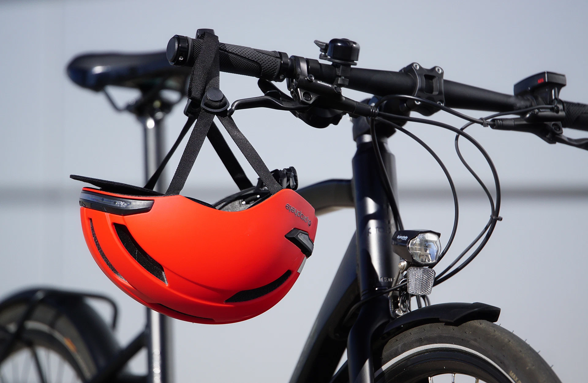 Fahrradhelm rot hängt an Fahrradlenker vor grauem Hintergund
