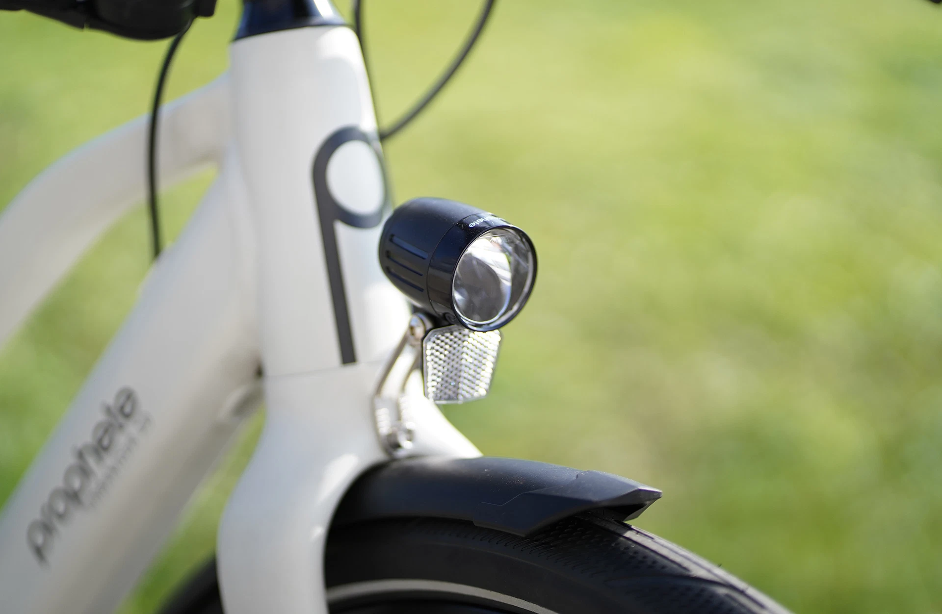 Bildausschnitt LED-Frontleuchte, Logo und Teilen vom Rahmen vor grasigem Hintergrund