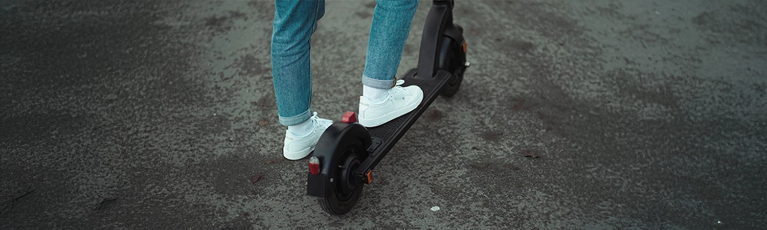 Bildausschnitt Trittbrett Prophete E-Scooter mit Person im Anschnitt. Man sieht weiße Sneakers und Jeans vor asphaltiertem Untergrund