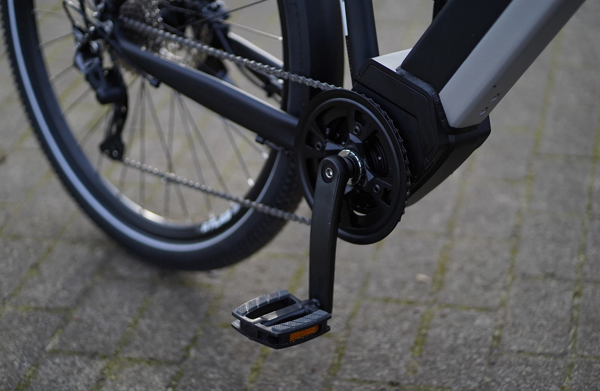 Bildausschnitt Detailaufnahme Mittelmotor, Kurbelgarnitur mit Pedalen und Kette auf gepflastertem Untergrund