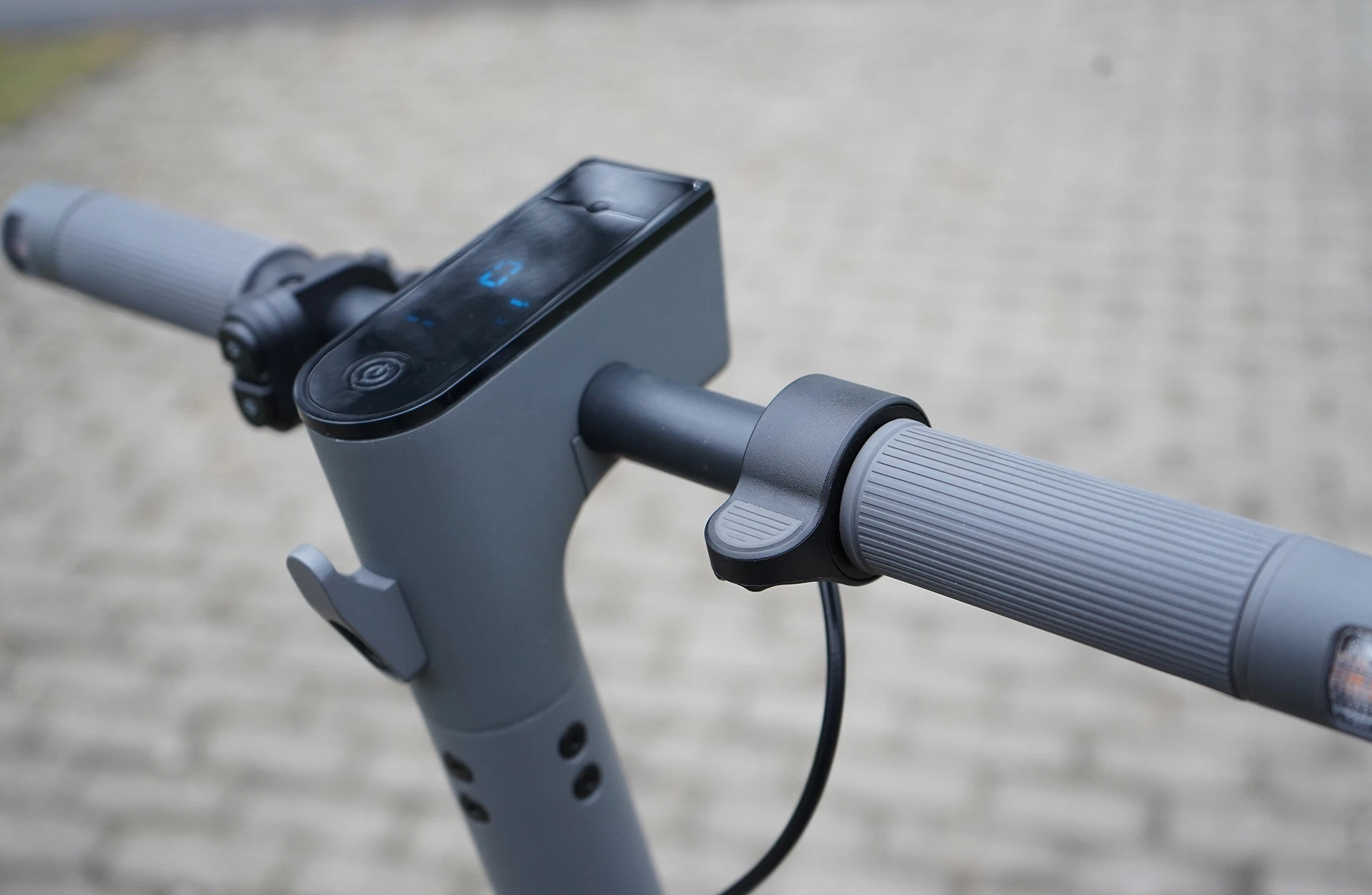 Bildausschnitt Lenker Prophete e-Scooter TWO mit grauen Griffen, Gashebel rechts und integriertem schwarzen Display in der Lenkstange vor unscharfem Untergrund