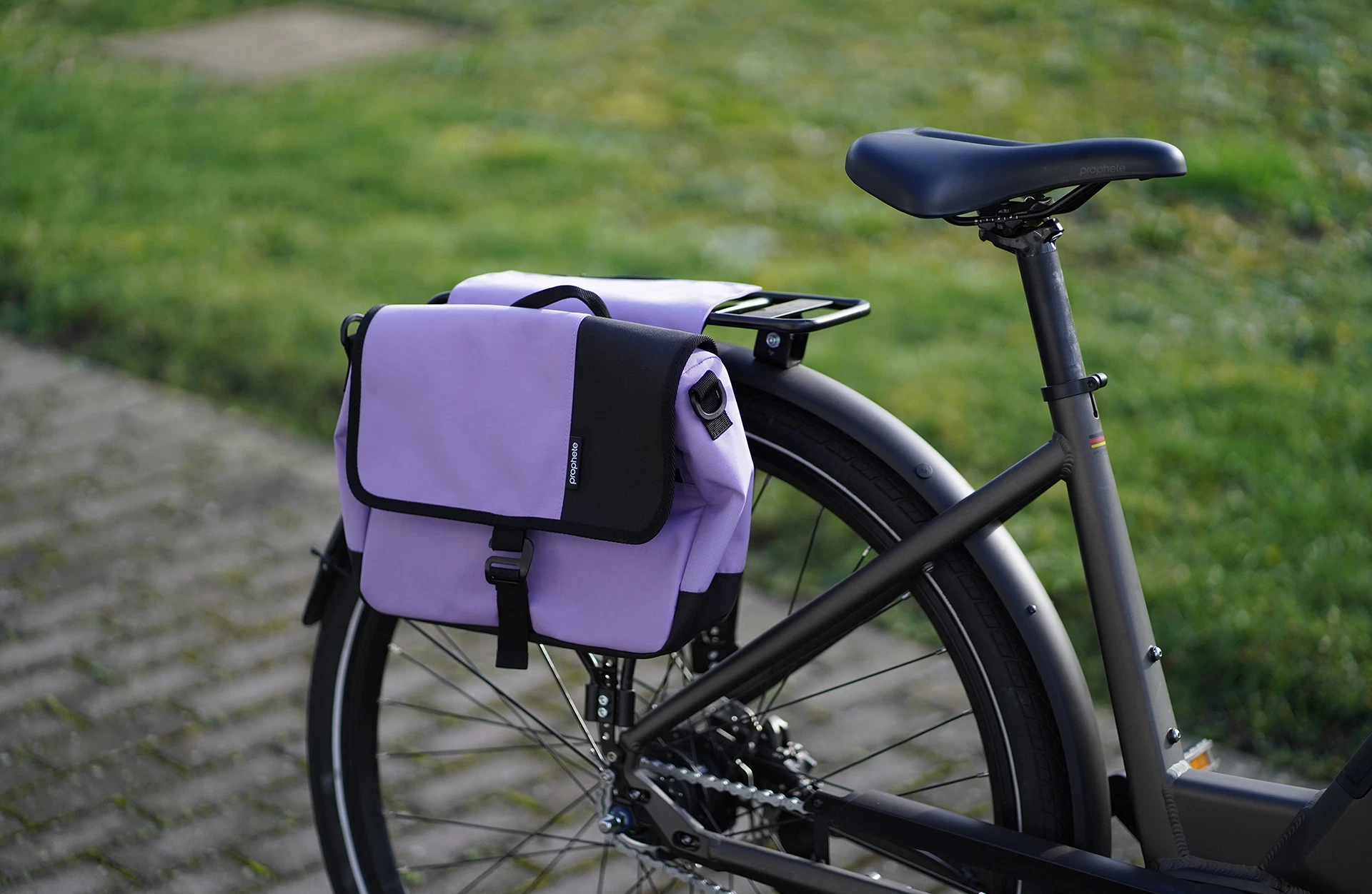 Seitenpacktasche lila am Heckgepäckträger mit Rahmen im Anschnitt vor Rasen und Pflastersteinen im Hintergrund