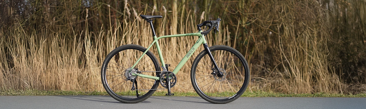 Vollansicht seitlich Prophete Graveler Gravelbike mit Dropbar Rennradlenker auf Straße vor natürlichem Hintergrund