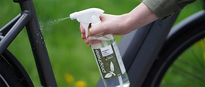 Hand sprüht Prophete Fahrradreiniger auf den Rahmen eines E-Bikes.